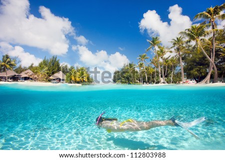 Woman swimming underwater in clear tropical waters in front of exotic 