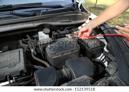 Car mechanic uses battery jumper cables to charge dead battery - stock 