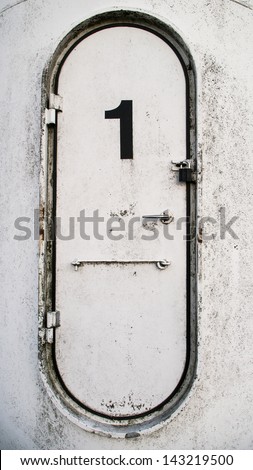Dirty white oval metal door with the number 1 written on it - stock 