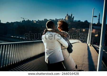 SAYKA stock photo stylish beautiful rich bride and groom walking and hugging on a sunny day on the bridge in the 266016428