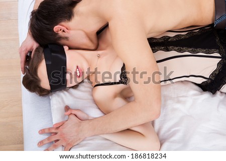 Side view of young man kissing sexy blindfolded woman in bed at home - stock photo