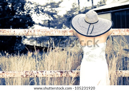 Back of a Woman wearing a big hat leaning on a rusted fence. Photo in
