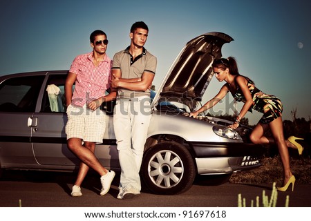 girl fixing car engine while couple of young man waiting by the car 