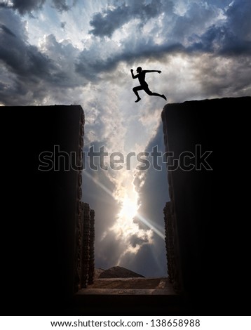 Man Silhouette jumping over the abyss at sunset cloudy sky background - stock photo