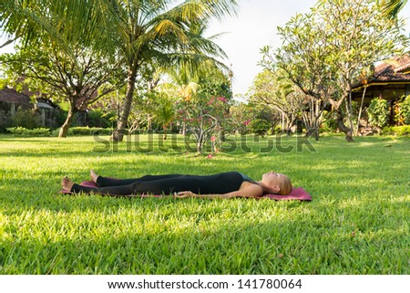 Shavasana. Young woman doing yoga exercises in the lush tropical garden - stock photo