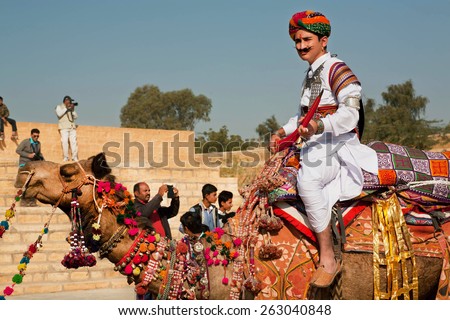 JAISALMER, INDIA - MAR 1: Camel rider in colorful dress goes past the tourist crowd of popular Desert Festival on March 1, 2015 in Rajasthan. Every winter Jaisalmer takes the Desert Festival - stock photo
