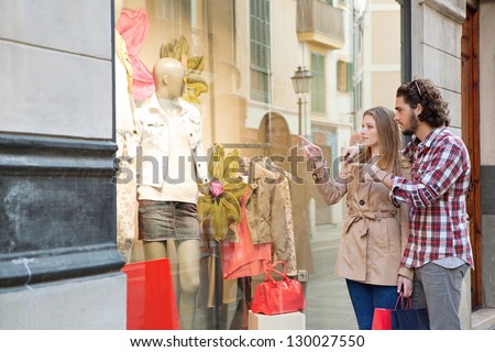 Young bohemian couple looking at clothes in a store window while on