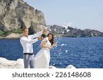 Small photo of couple uncorking champagne bottle by the sea after their wedding