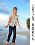 Small photo of Full growth portrait on a tropical beach: handsome 8 years old boy in wet clothes without shoos ankle-deep in water. Boy runs