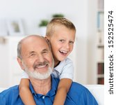Laughing grandfather with his grandson as they play together indoors in the living room with the cute young boy hugging him from behind - stock photo