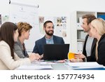Smiling manager with his business team sitting discussing a project with them around a table with a laptop in front of him - stock photo