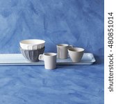 Small photo of Handmade blue crockery set against rustic blue painted wall.