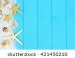 stock-photo-summer-side-border-of-sand-sea-shells-and-star-fish-on-blue-wooden-background-421450210.jpg