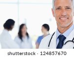 Doctor showing a beaming smile with his medical interns behind him - stock photo