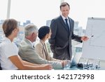 Smiling businessman pointing at whiteboard during a meeting with colleagues listening to him - stock photo