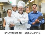 Head chef posing with the team behind him in a professional kitchen - stock photo
