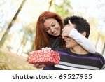 woman covering the eyes to his boyfriend with giving him a present (selective focus with shallow DOF) - stock photo