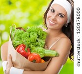Portrait of happy smiling young beautiful woman in fitness wear holding grocery shopping bag with healthy vegetarian food, outdoors - stock photo