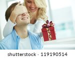 Image of young female with giftbox closing her boyfriend eyes to make a surprise for him - stock photo