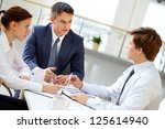 Serious boss looking at one of his employees and listening to him at meeting - stock photo