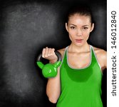Fitness woman exercising crossfit holding kettlebell strength training biceps. Beautiful sweaty fitness instructor on blackoard background looking intense at camera. Asian Caucasian female model. - stock photo
