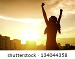 Happy successful sportswoman raising arms to the sky on golden back lighting sunset summer. Fitness athlete with arms up celebrating goals after sport exercising and working out outdoors. Copy space. - stock photo