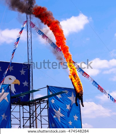 Fire Diver Performing off the high dive platform head first into a pool of water at a show. Stuntman is dressed in a black fire protecting outfit. A very dangerous yet exciting athletic sport stunt.