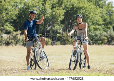 Happy senior couple cycling in the park. Senior man pointing to mature woman the way to choose for a bike trip. Happy cyclist biking in a summer day.