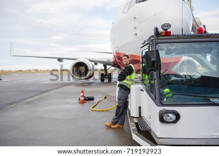 Worker Leaning On Towing Truck With Airplane In Background