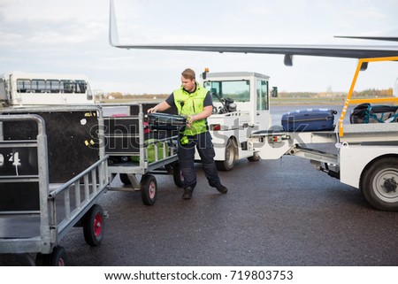 Male Worker Placing Luggage In Trailer On Runway