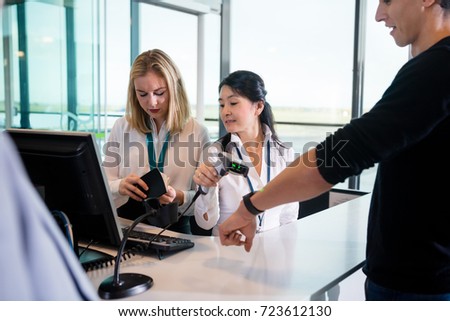 Receptionist Scanning Passengers Smart Watch While Colleague Che