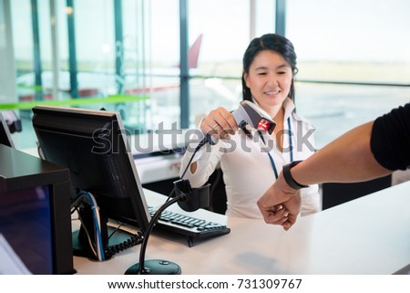Smiling Receptionist Scanning Smart Watch Of Passenger At Airpor