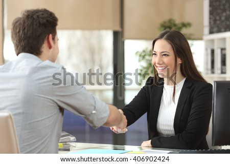 Happy businesswoman handshaking with client closing deal in an office interior with a window in the background