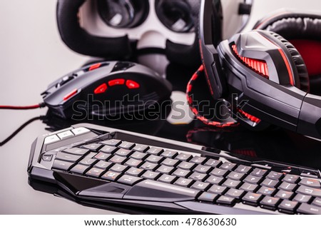 a gaming keyboard, mouse, headset and Virtual reality glasses shot over a dark reflective surface