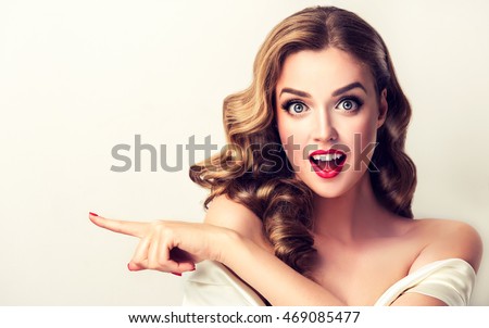 Người phụ nữ ngạc nhiên cho thấy sản phẩm cô gái .Beautiful với mái tóc xoăn trỏ đến một bên. Trình bày sản phẩm của bạn. Bị cô lập trên nền trắng. biểu thức biểu cảm trên khuôn mặt