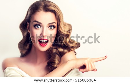 Woman surprise showing product .Beautiful girl with curly hair pointing to the side . Presenting your product. Isolated on white background. Expressive facial expressions