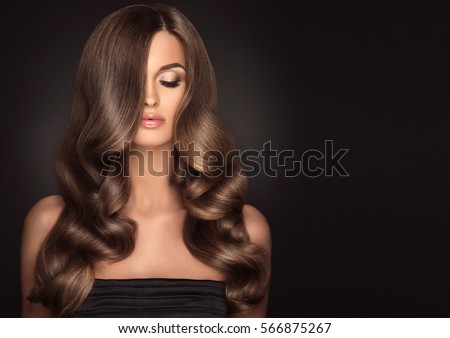 Brunette girl with long and shiny wavy hair . Beautiful model with curly hairstyle .