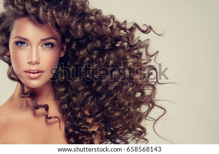 Brunette girl with long and shiny curly hair . Beautiful model woman with wavy hairstyle .