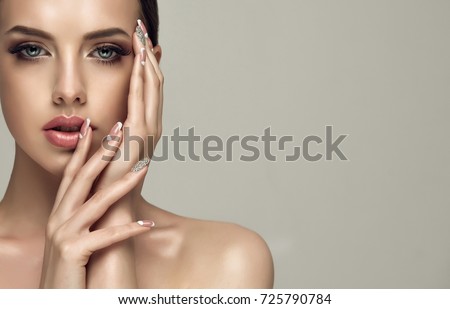 Beautiful model girl with a beige French manicure nail design with rhinestones . Fashion makeup and care for hands and nails and cosmetics .