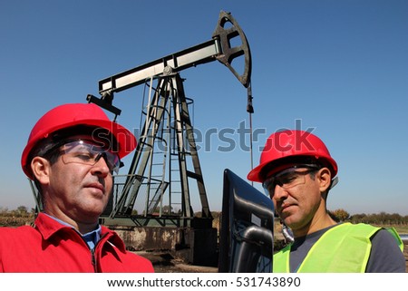 Petroleum Engineers Looking at Laptop Computer / Petroleum engineers next to pump jack in the oil field working with laptop