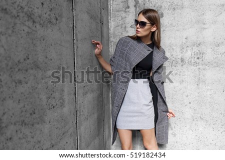 high fashion portrait of young elegant woman outdoor. Grey coat, cat eye sunglasses, grey wall background