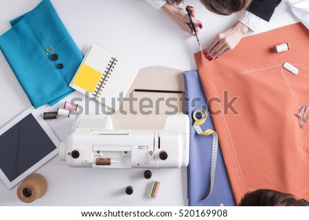 Top view of woman holding scissors and red material with pattern drawn on it about to start cutting and sewing