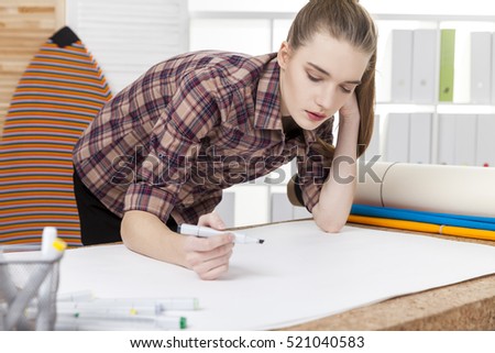 Serious woman designer is bent at her table and starting to sketch a new project. Concept of creative work