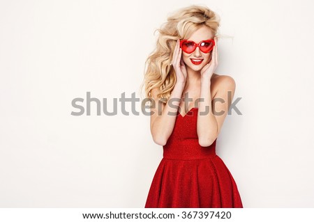 valentine's day portrait of an attractive young blonde girl with heart shaped glasses in red dress