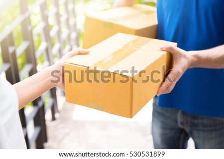 Delivery man in blue uniform handing parcel box to recipient - courier service concept