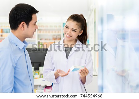 Beautiful Asian female pharmacist or doctor explaining prescription medicine to a male customer in a pharmacy.