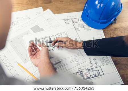 Engineer and architect team discussing floor plan layout for new development in progress on site with blue safety helmet on table