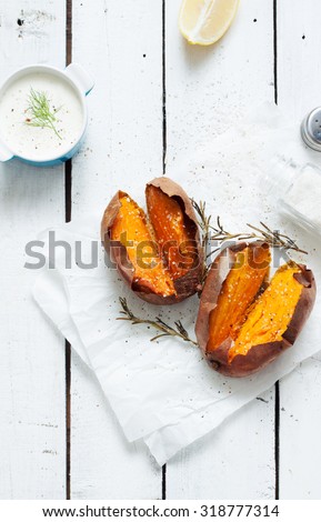 Baked sweet potatoes, dip, salt and rosemary. White wooden rustic picnic table scenery from above.