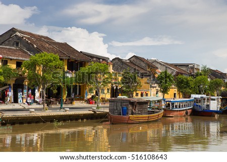 Wooden boats on the Thu Bon River in Hoi An Ancient Town (Hoian), Vietnam. Yellow old houses on waterfront.