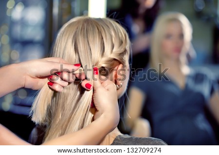 Hairdresser make French braids in beauty salon.